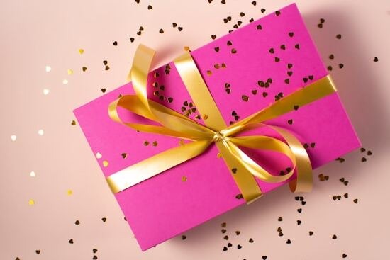 A bright pink gift box with a golden ribbon and confetti scattered around it, representing how the spirit of prophecy is a gift from God