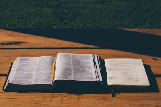 An open Bible and notebook lying on a wooden table.