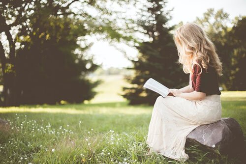 A woman reads her bible while sitting on a rock outside. The outdoors can be a peaceful place to study God's Word.