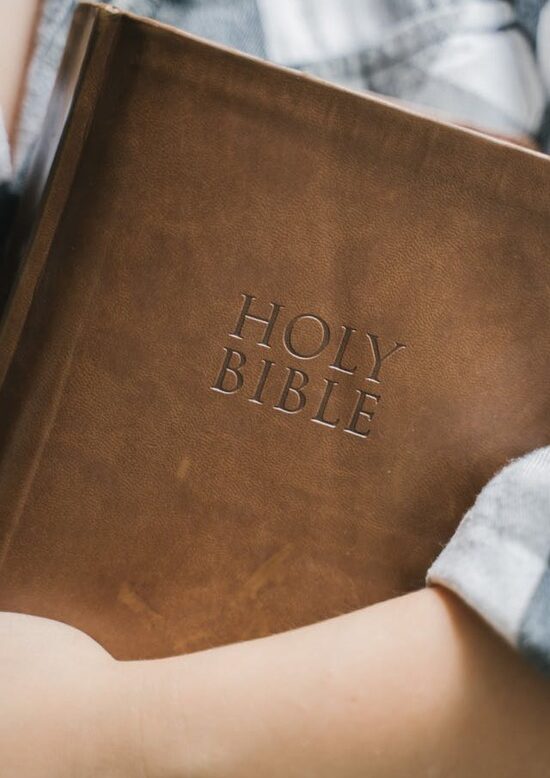 A person holds a Bible in the crook of their arm.