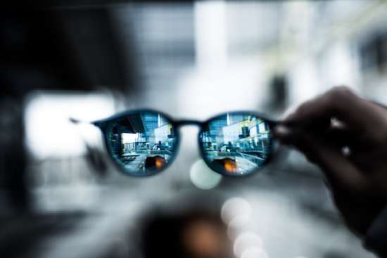 A person holding up eyeglasses, its lenses helping the blurry background come into focus.