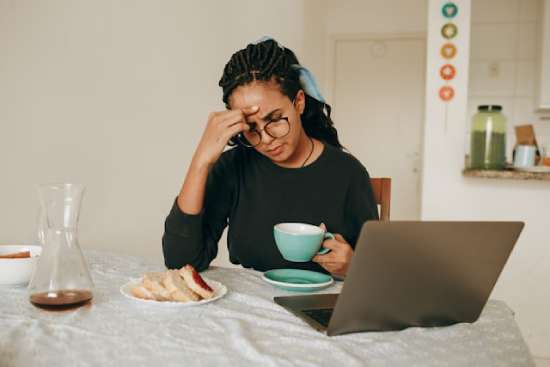 A woman eating breakfast by her computer as she ponders a difficult decision.