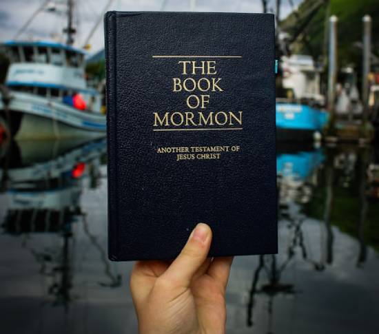 A woman's hand holding up a Book of Mormon, which came from Joseph Smith's visions.