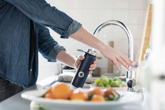 Woman filling up a water bottle at her kitchen sink.