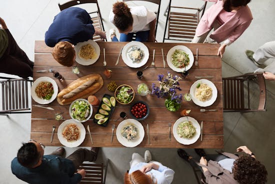 A group of friends gather around a wooden table with food. Sabbath is a great time to make connections while enjoying good food!