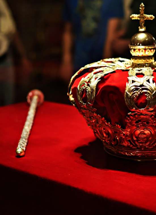 A royal crown and scepter resting on a red table.