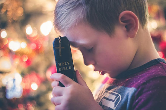 Young boy with Holy Bible praying with closed eyes as we explore what is prayer and what does it mean to pray