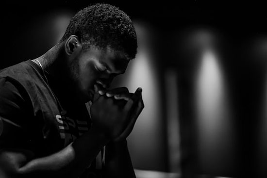 A man folding his hands and bowing his head in prayer as he asks God to provide for his needs.