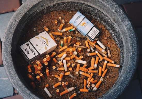 An ashtray full of cigarettes and cigarette boxes.