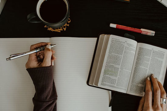 A woman's hand taking notes as she studies the Bible