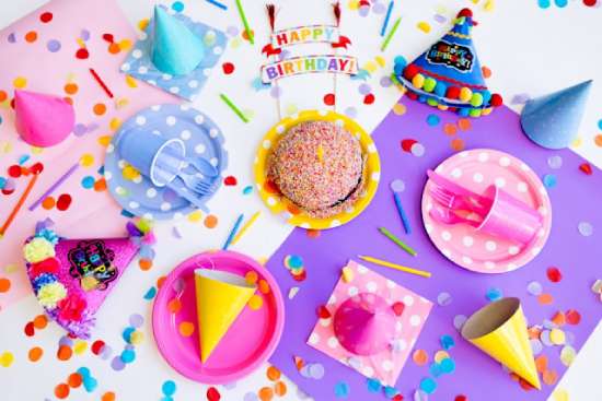 A table covered in pink and purple birthday party favors, hats, and confetti