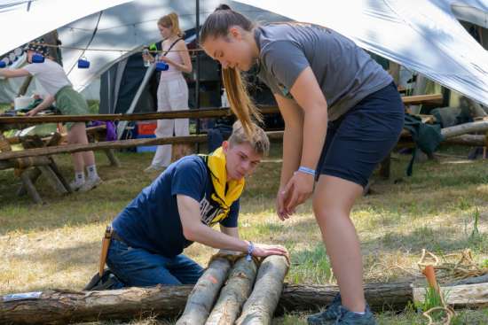 Two Pathfinders work together to arrange some logs. It looks as if they are constructing a shelter or foundation of some sort.