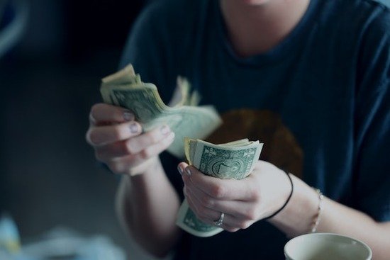 A woman holding dollar bills and counting out money for tithe