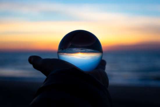 Hands holding a glass ball that is reflecting the ocean and the sunset