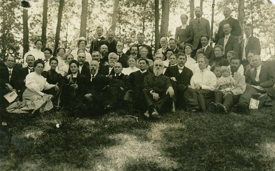 A black and white photo of Ellen G. White with a group of people in Australia. They are in a wooded area, most sitting in the grass and some standing.