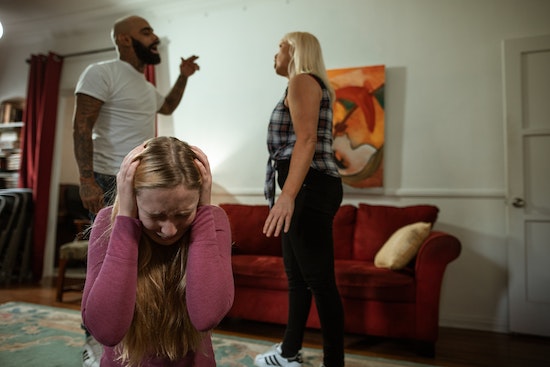  A girl holding her hands over her ears while parents argue in the background