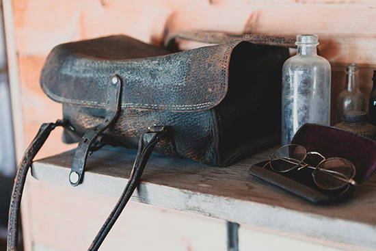 A leather doctor's bag, a glass bottle, and a pair of glasses sitting on a shelf.