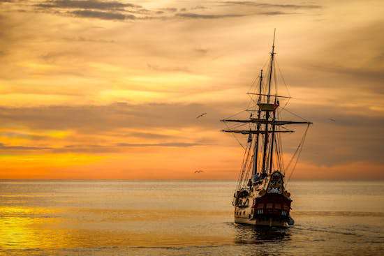 A wooden ship sailing into a sunset