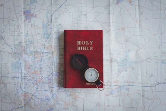 A red Bible and compass on top of a map, symbolizing how the Bible is our guide