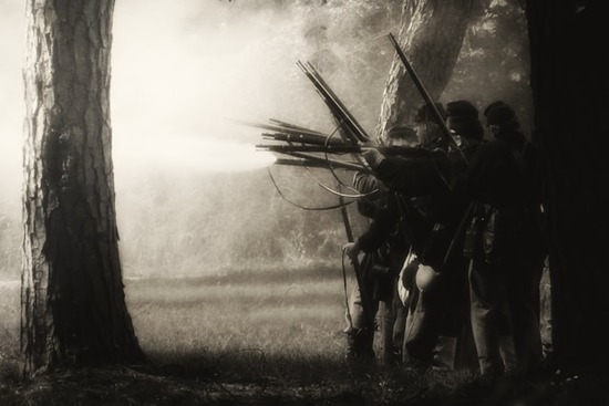 A black and white photo of civil war soldiers lined up and firing at the enemy.