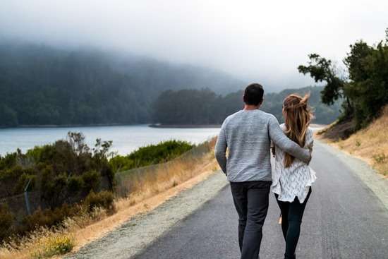 A couple walking along a road with the man's arm around the woman