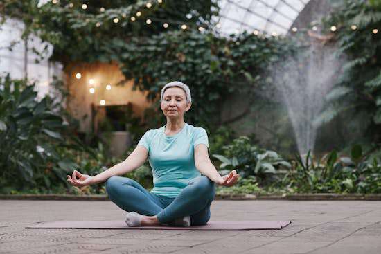 A woman meditating with folded legs and outstretched arms.