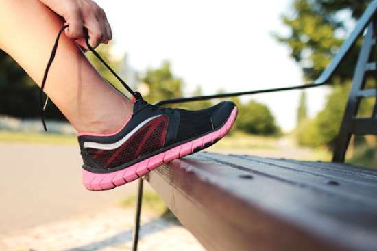 A woman ties her shoe on a bench before she starts exercising.