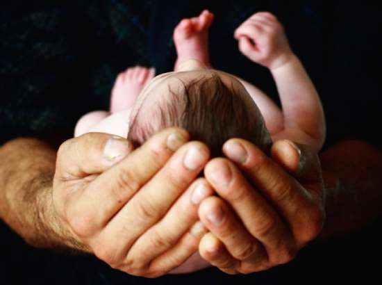 An infant child resting in their parent's hands.