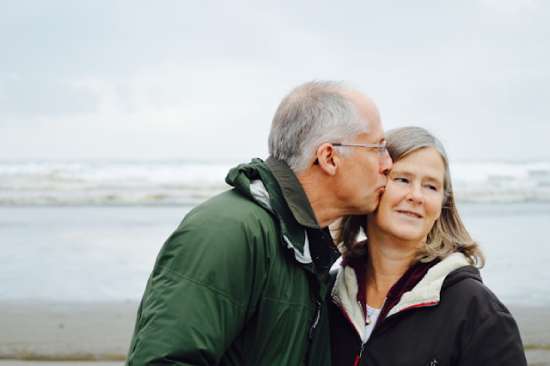 An older man kissing the cheek of his wife as they enjoy good health and time on the beach together