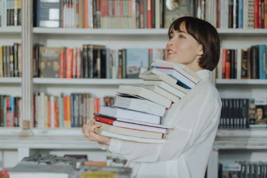 Woman carrying a stack of books in a bookstore