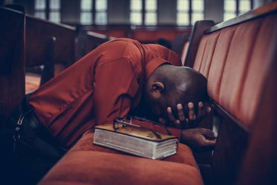 A man kneeling in church with his head in his hands, asking God to help him in his relationships