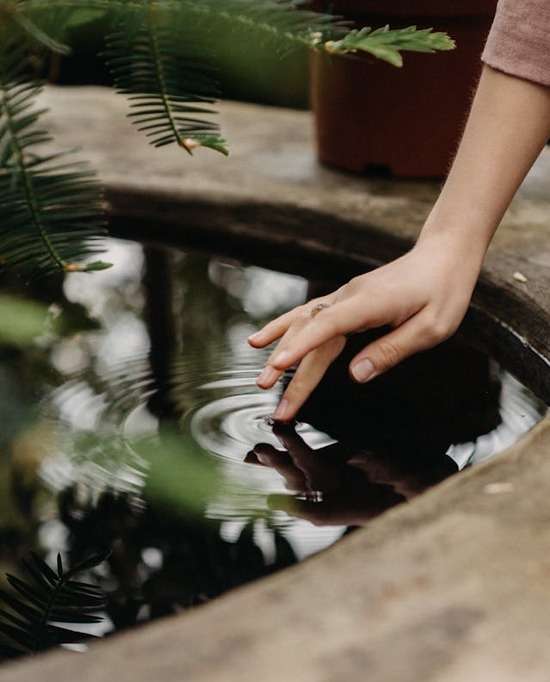 A woman touching a finger to a pool of still water