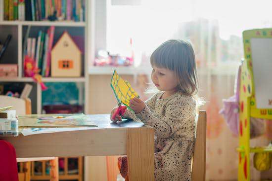 A young girl sitting at a table, cutting paper as a craft for school 