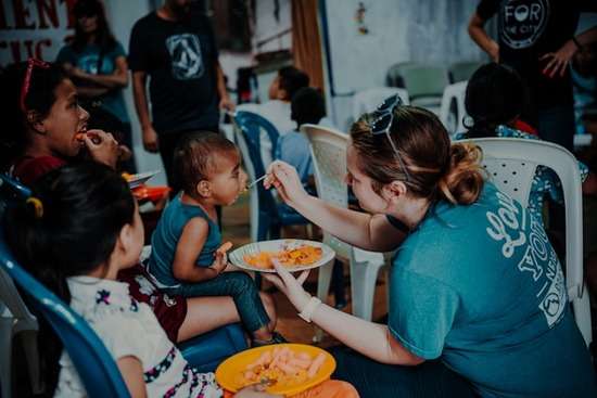 A woman feed a spoonful of food to a impoverished child