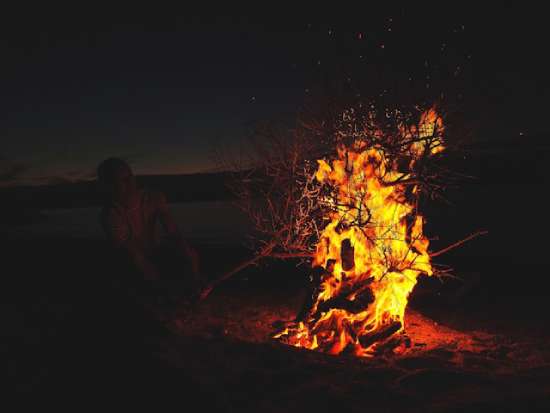 A person adding tree branches to a fire in the desert at night.