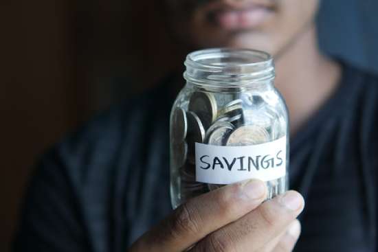 A person holding a jar of coins as part of their savings.