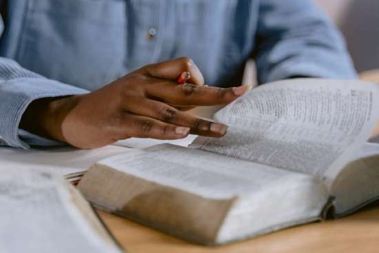 A person flipping through a Bible, pencil in hand