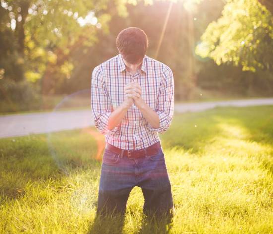 A man kneeling in the grass while praying illustrates what it may look like for someone to accept Christ's gift of salvation.